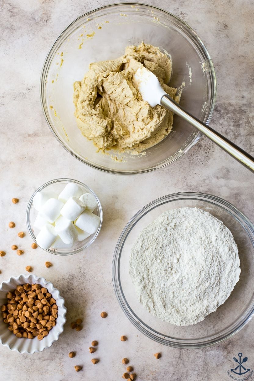Overhead photo of dough for blondie bars in a glass bowl with a bowl of flour, a bowl of large marshmallows and a bowl of butterscotch morsels
