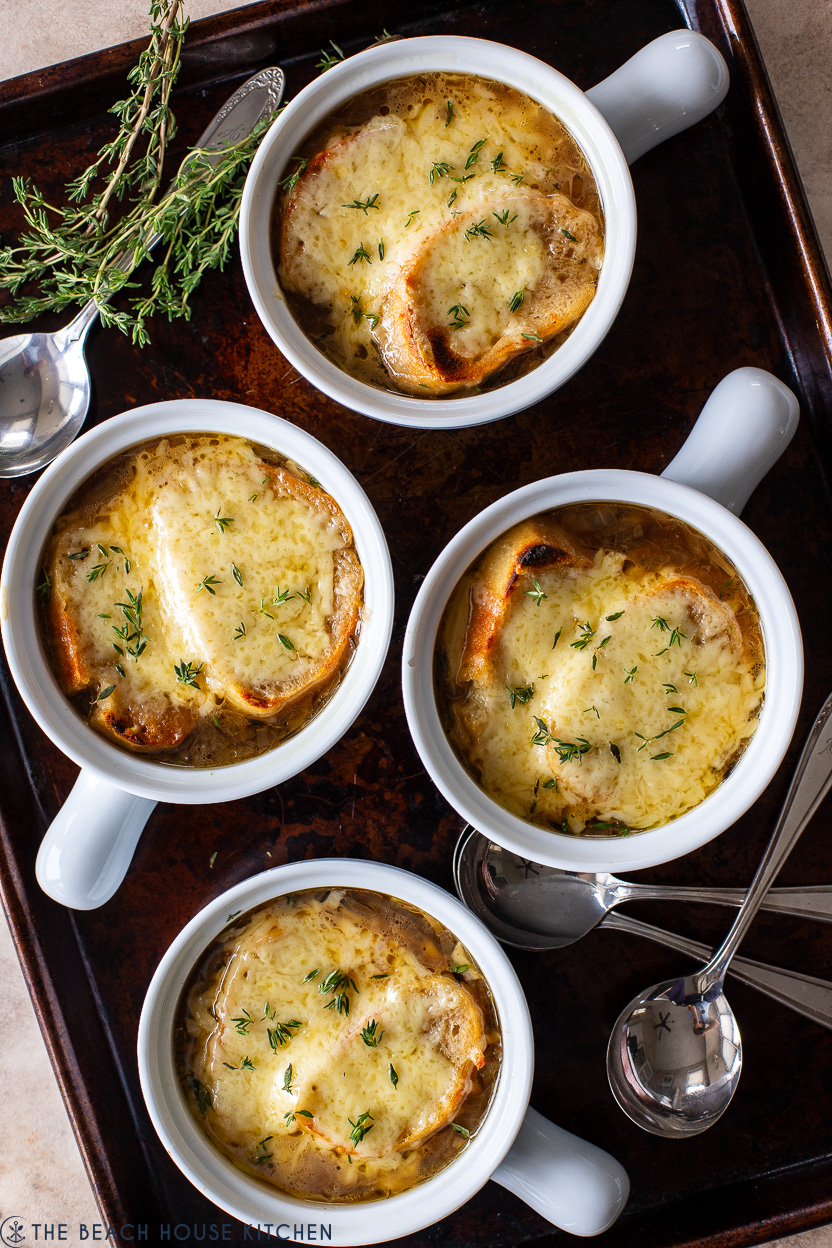 Overhead photo of a baking sheet topped with four crocks of French onion soup with some spoons and fresh thyme sprigs