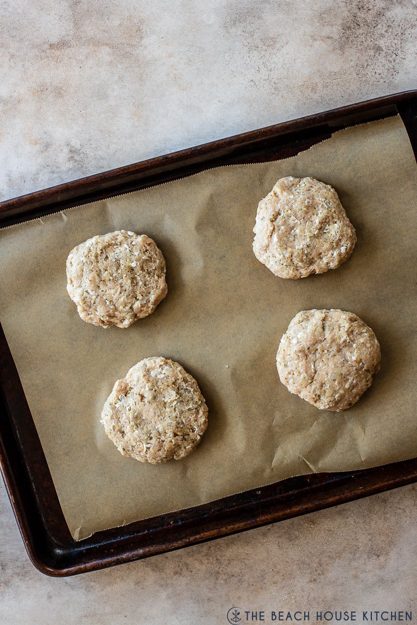 Overhead photo of a baking sheet of four pre-cooked chicke burgers