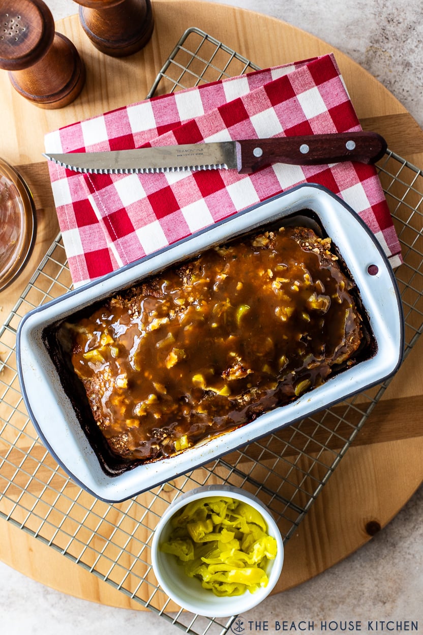Overhead photo of a Mississippi Meatloaf in a loaf pan on a wire rack with a red and white check napkin.