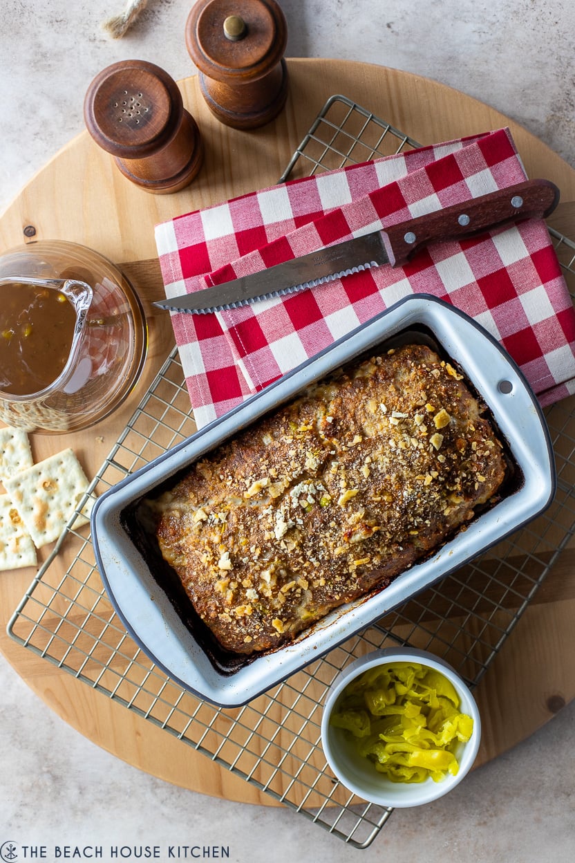 Overhead photo of a cooked meatloaf on a wire rack with a red and white chcekd napkin