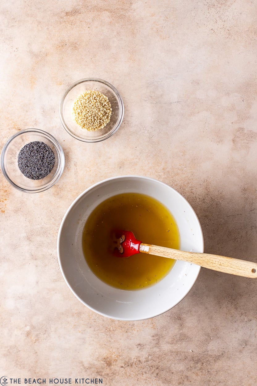 Overhead photo of a bowl of melted butter and two small bowls of sesame seeds and poppy seeds.