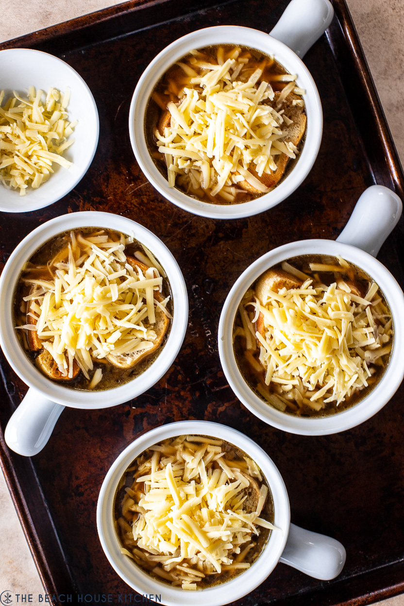 Overhead photo of four crocks of French Onion Soup on a baking sheet topped with shredded cheese