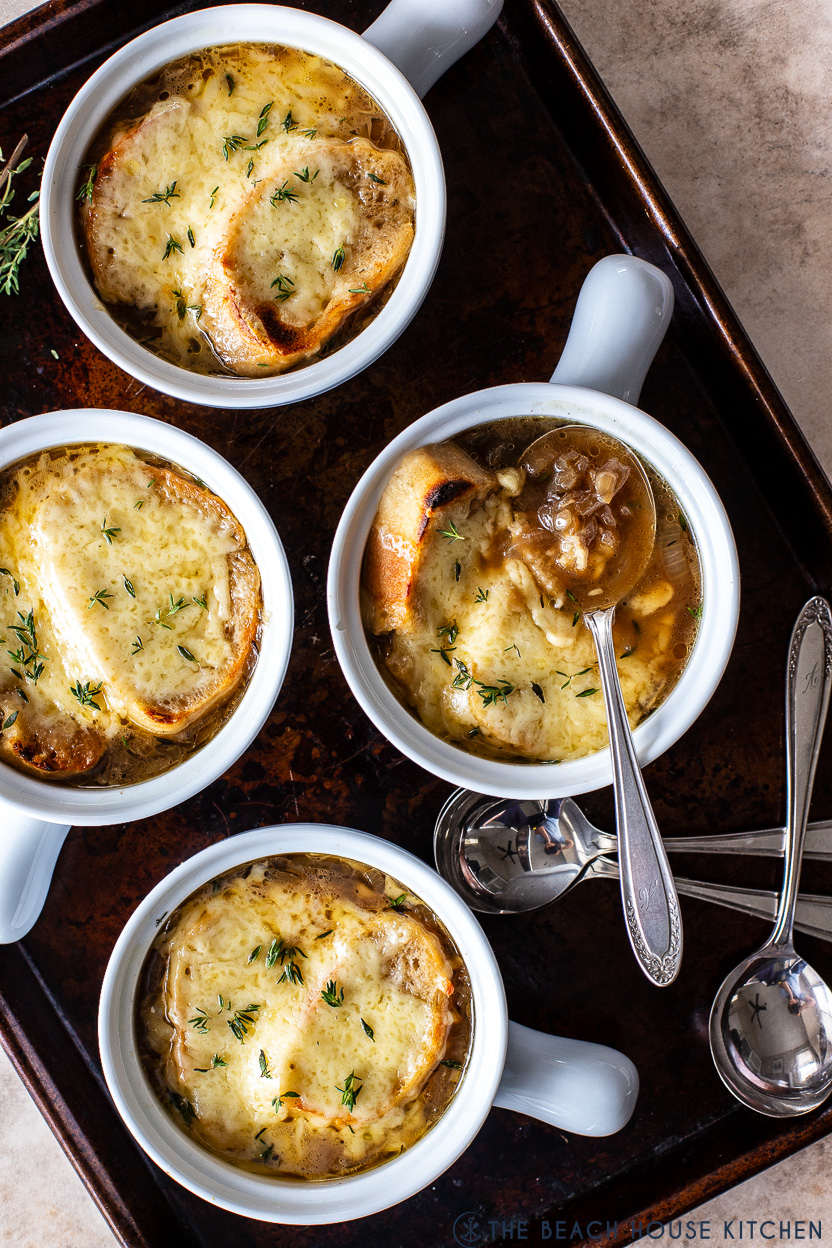 Overhead photo of four crocks of French onion soup on a baking sheet with a few spoons